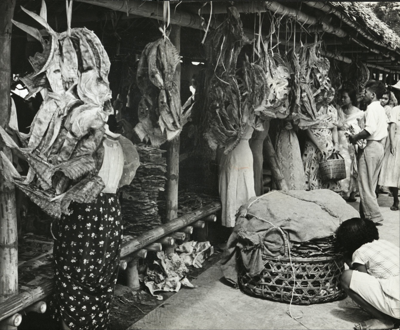 336. PHILIPPINES: Shopping for dried fish in a Baguio market. The covered basket in fore-front also contains this food.