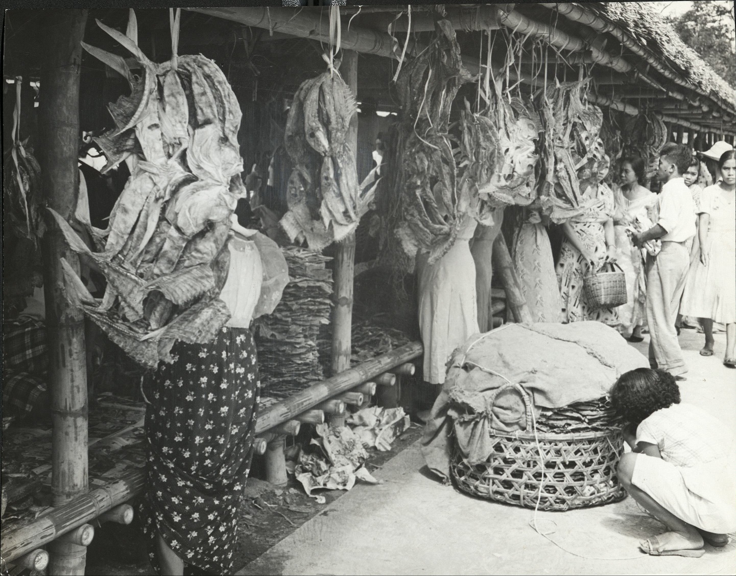 336. PHILIPPINES: Shopping for dried fish in a Baguio market. The covered basket in fore-front also contains this food.