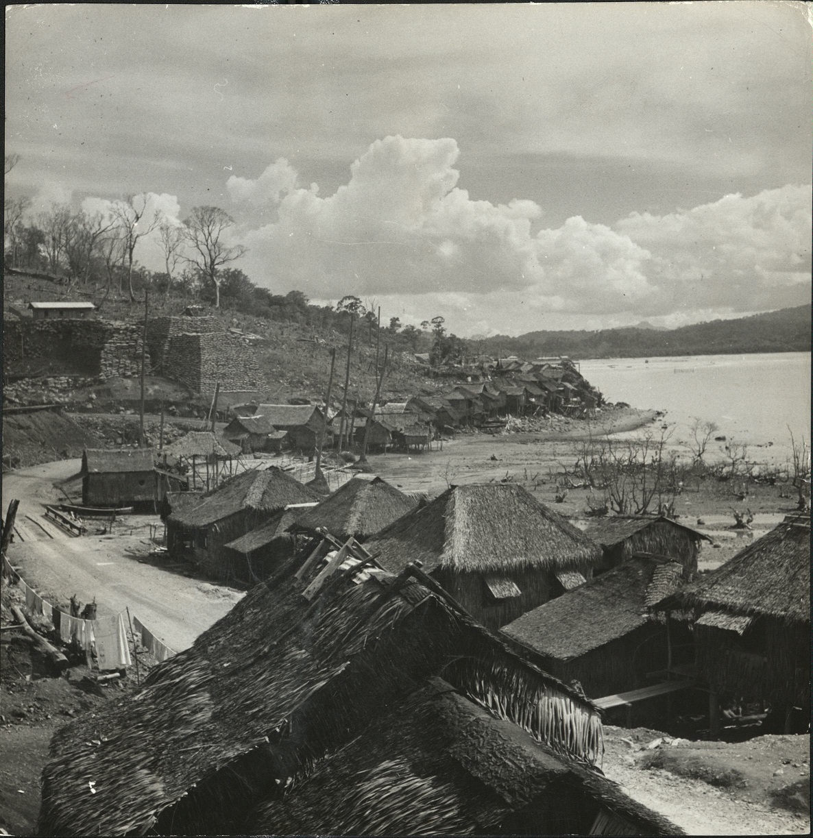[Caption missing – Village by bay or river with denuded trees].