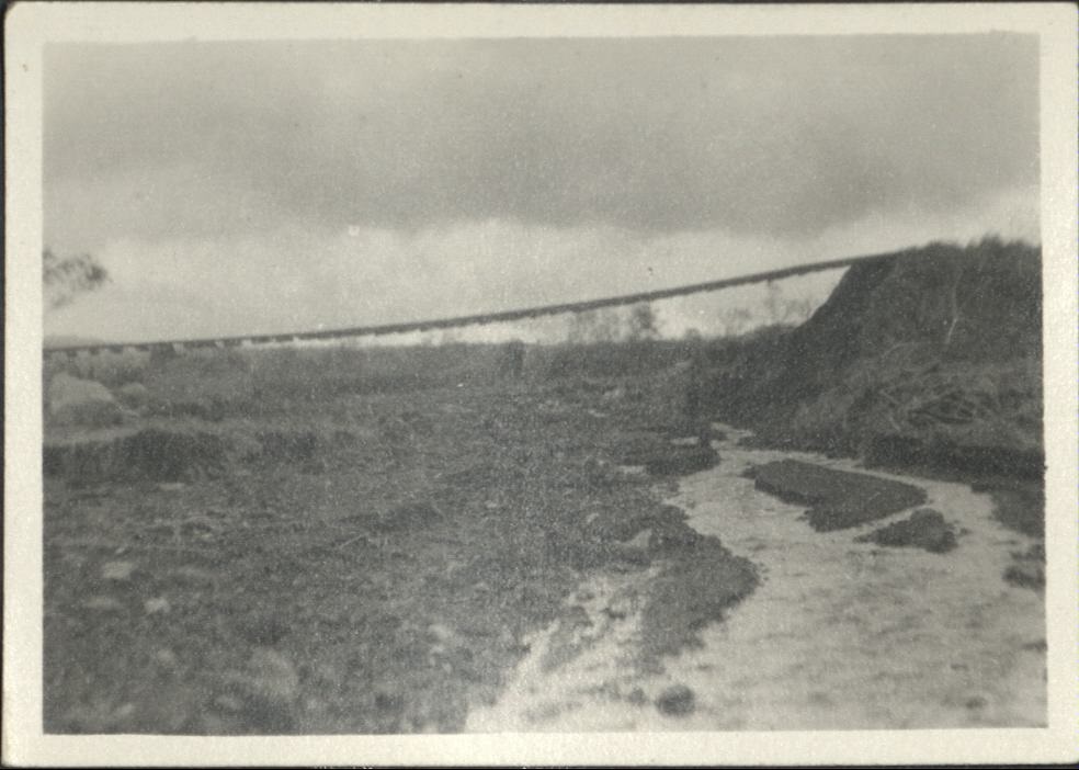 [Untitled – Washed-out bridge and  railroad tracks hang over dirt and rocks after a flood or landslide].