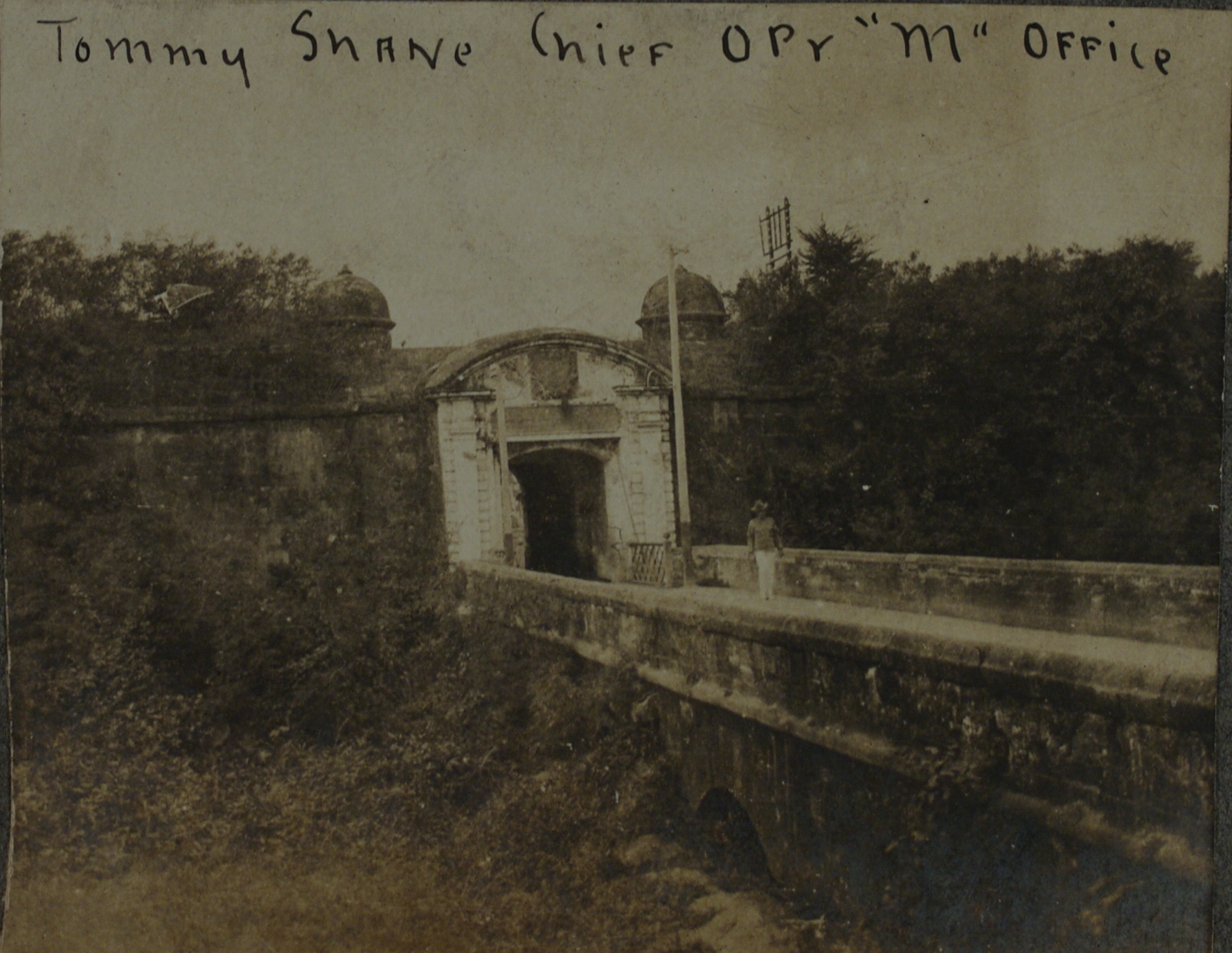 Tommy Shane, Chief Opr. [Operator] “M” Office [posing at Intramuros gate Revellin de Real de Bagumbayan].