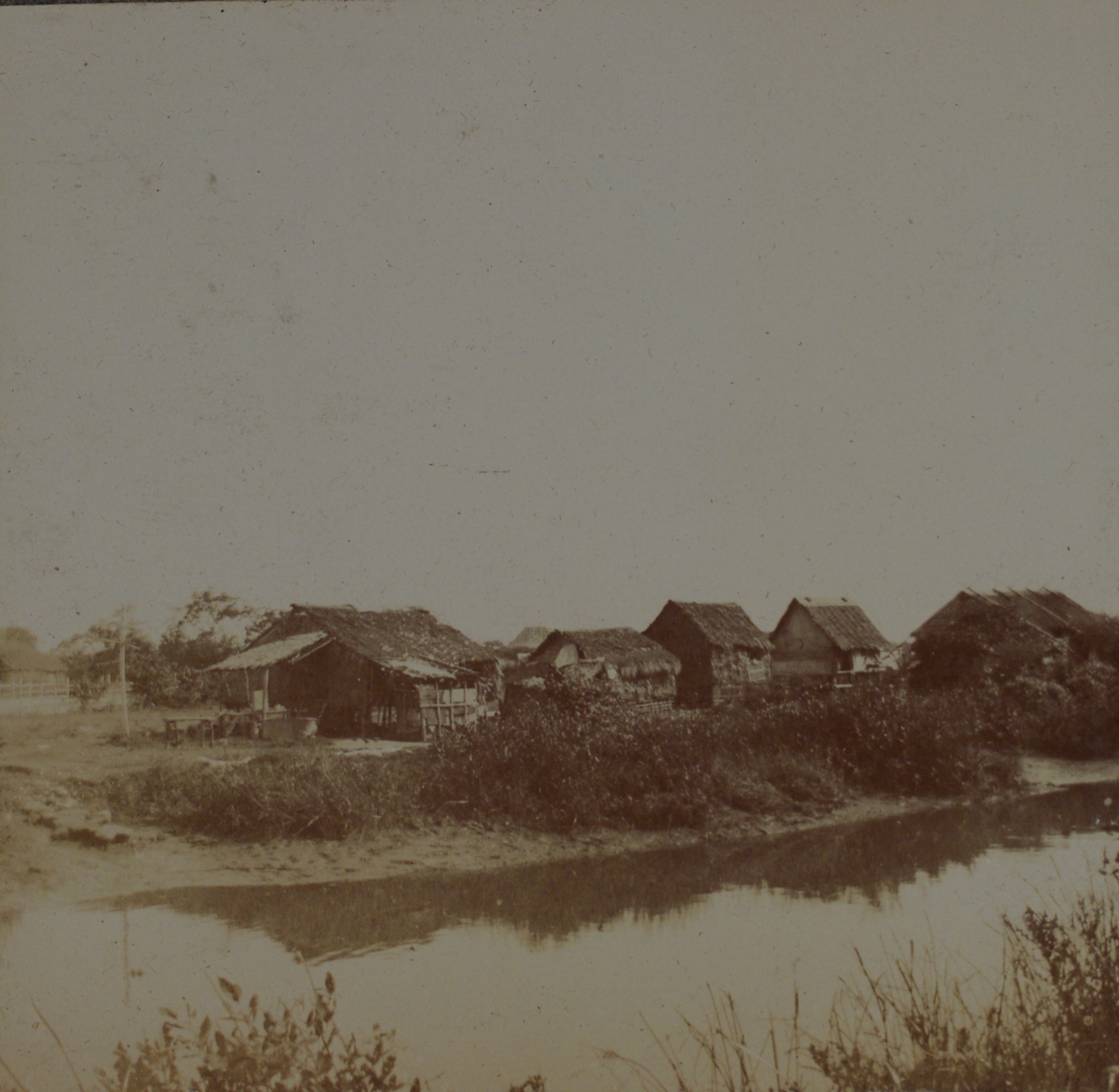 [Untitled – Nipa buildings by a river].