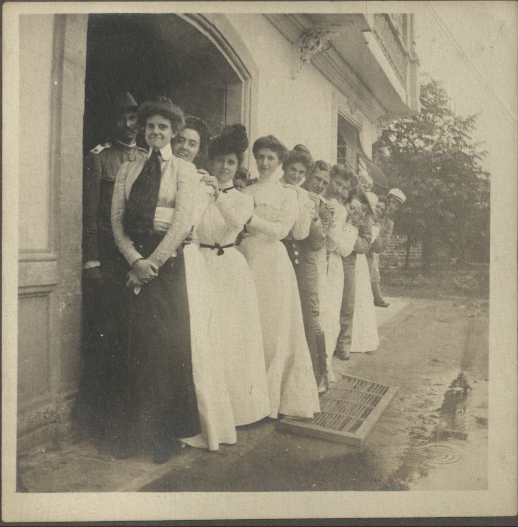 [Untitled – Line of expatriates, mostly women, under house eaves].
