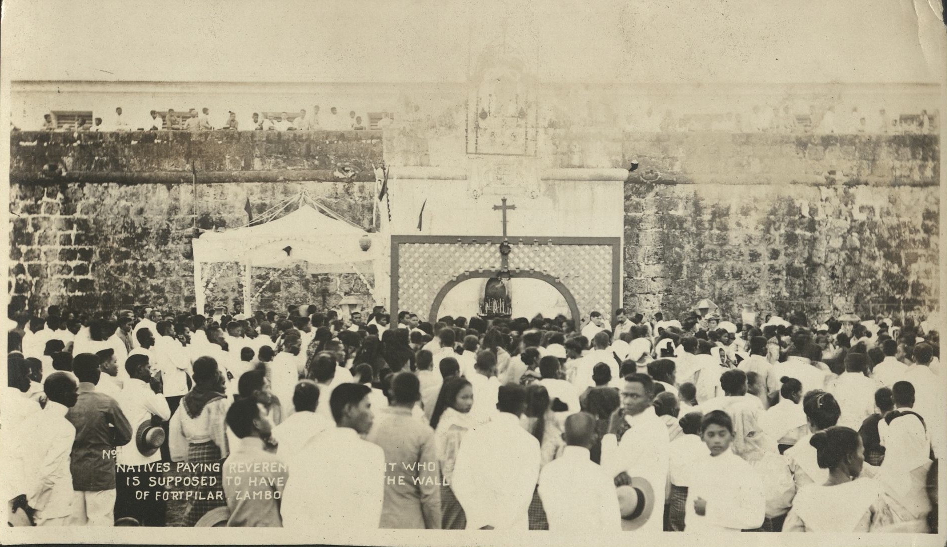 Natives paying reverence (illegible) who is supposed to have (illegible) the wall of Fort Pilar, Zamboanga.