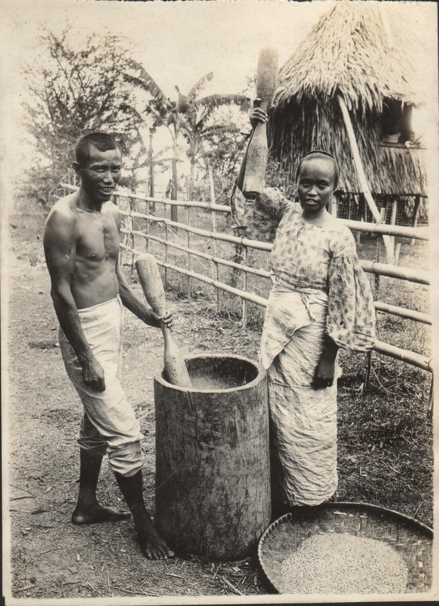 Man and woman pounding rice with pestles in a wooden mortar to loosen hull.  Bigao [Bigaa, now Balagtas], Bulacan Province.