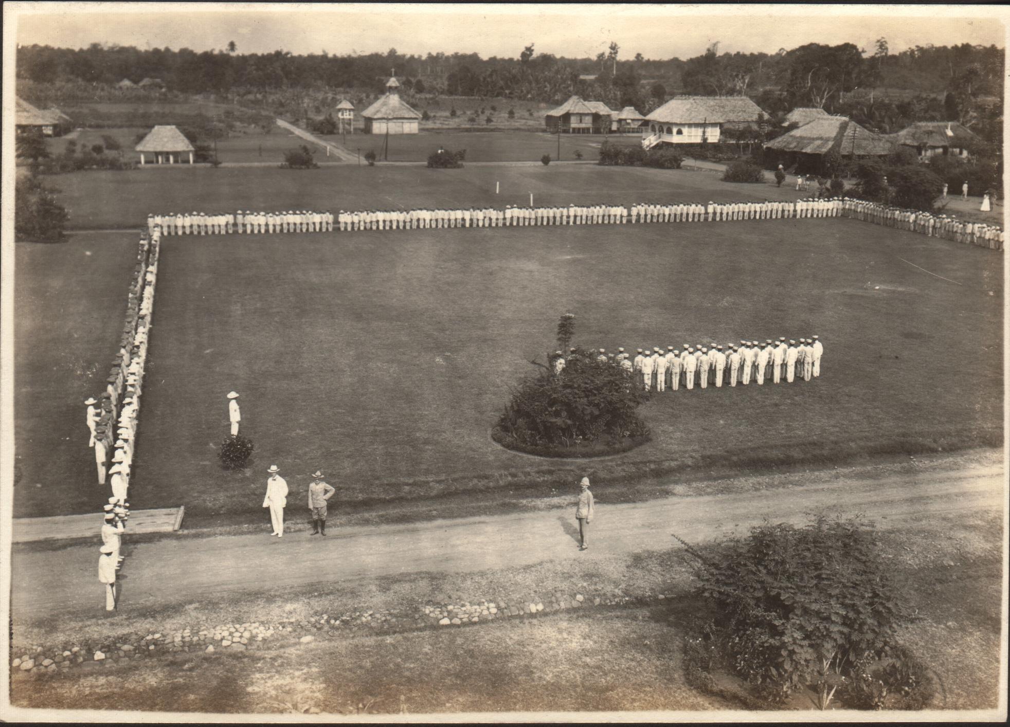 View of the parade grounds [at Iwahig Prison] with prisoners lined up for inspection.