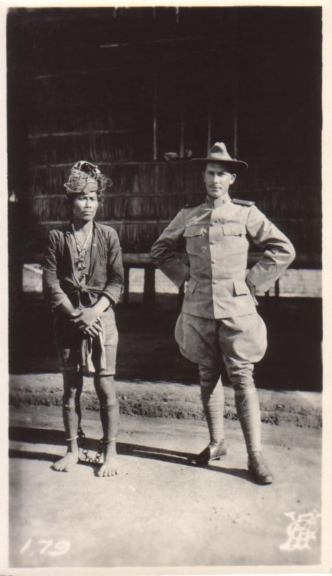 [Untitled – An indigenous man in ankle irons stands before a nipa structure with an American officer].