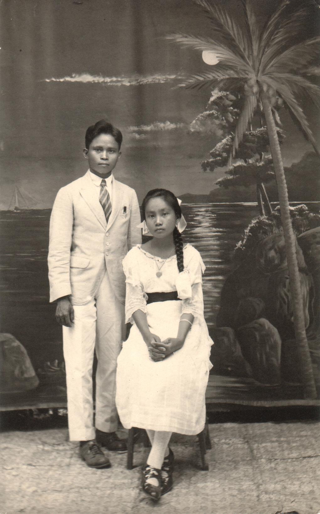 [Untitled – Studio portrait of young man and young woman posing before a painted tropical moonlight backdrop].